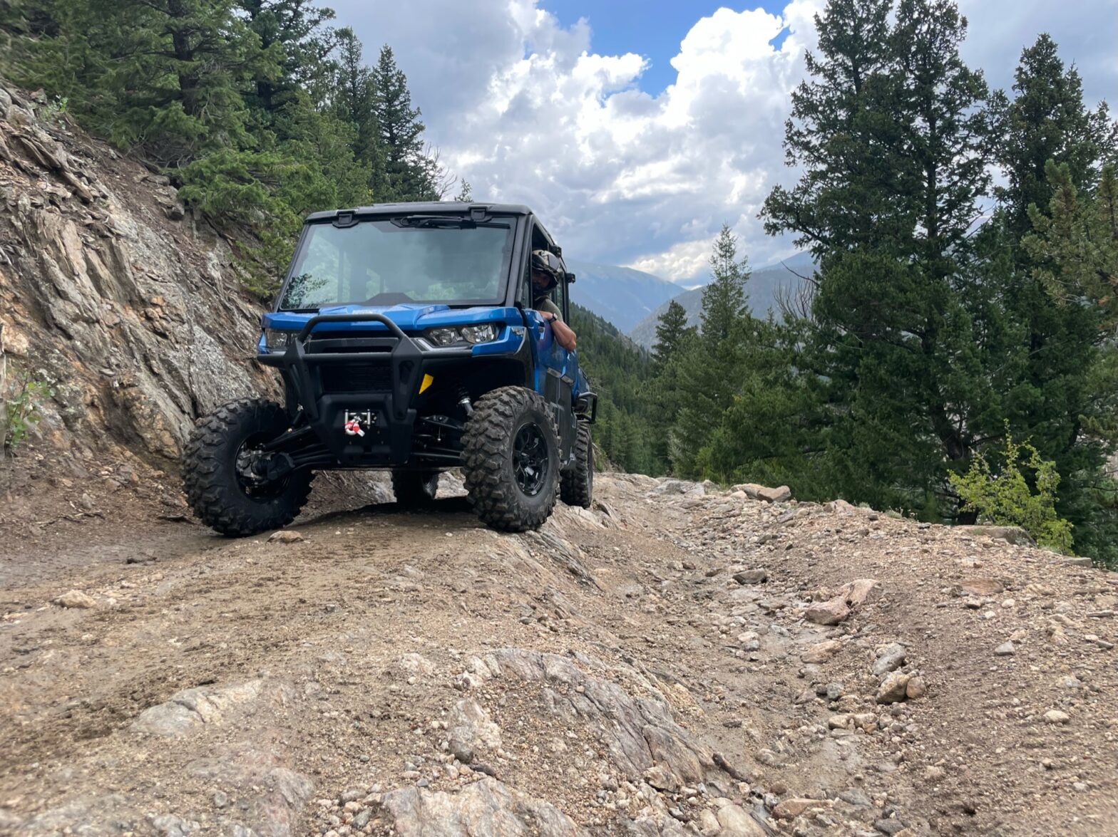 UTV on a trail in Colorado with pine trees and mountains in the background